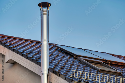 A stainless steel chimney and parts of a roof with solar panels at dusk.