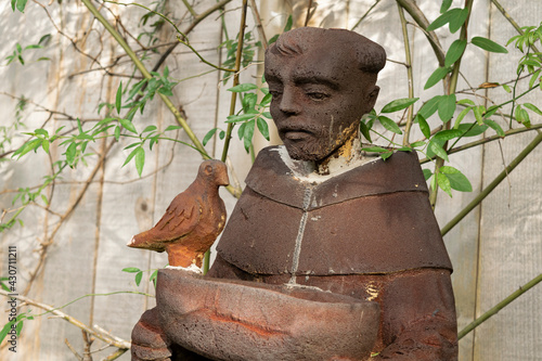 A bird bath statue of St. Francis of Assisi in a backyard garden.