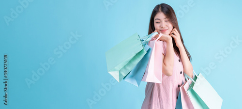 portrait of cheerful young brunette woman holding credit card and shopping bags over Blue background. shopaholic Concept