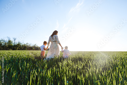 A mother with two daughters is walking in a green field. Hugs and feelings.