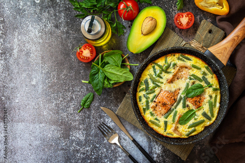 Breakfast or lunch snack concept. Rustic omelet (omelette, Scrambled) with salmon fillet and green beans in a frying pan on a stone background. Top view, flat lay. Copy space.