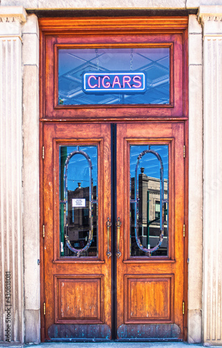 Vertical vintage double wooden doors with transom window with CIGAR sign hanging and old fashioned panels on ceiling visible in classical building