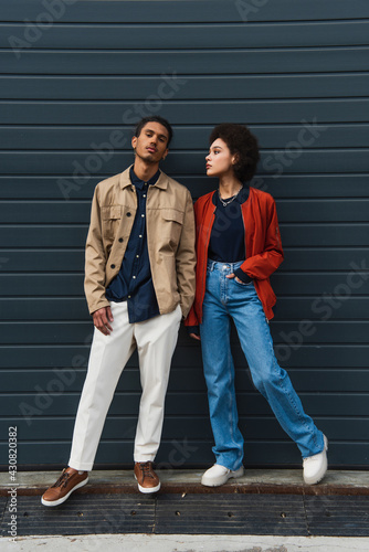 full length of young african american man posing with stylish woman standing with hand in pocket
