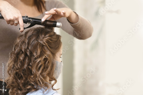 A lock of brown hair in the hands of a barber master with curling iron. The concept of a hairdresser, hair styling. Copy space.
