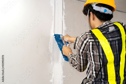 Construction worker plastering gypsum board or plasterboard panels wall with trowel. Home interior drywall works, renovation or construction