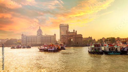 Sunset photo of city scape with The Gateway of India along with Taj and boats as seen from the Mumbai Harbour in Mumbai, Maharashtra India with a beautiful warm sky.