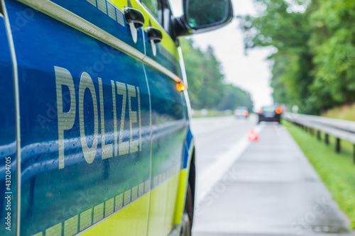 Police car on the highway in a side perspective during an accident. Lettering police on the body with boom and yellow background. Hard shoulder, lane and crash barriers with trees