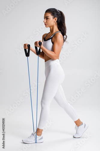 Fitness woman working out with resistance band on gray background. Athletic girl exercises with expander