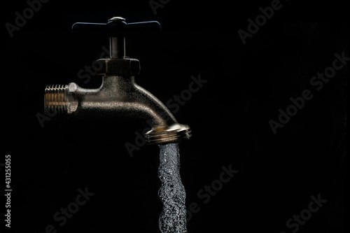 low key light of faucet witrh water flow in black back background