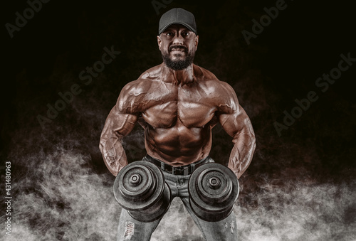 Muscular athlete lifts dumbbells. Shoulder pumping. Fitness and bodybuilding concept.