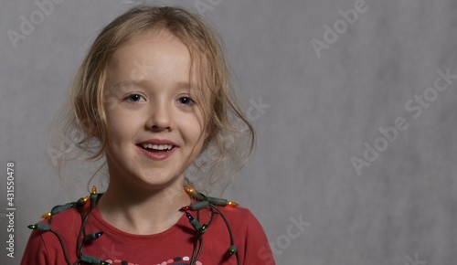 Śliczna dziewczynka w wieku przedszkolnym, w czerwonej bluzce, siedzi, jasne tło, portret horyzontalny. 
