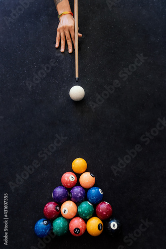 The hand of a man with a billiard cue aims at a billiard ball