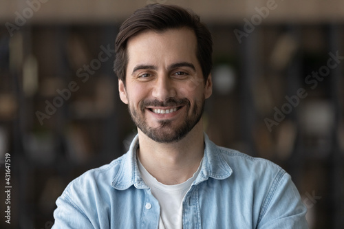 Head shot portrait smiling confident millennial man looking at camera, standing at home, happy positive bearded young male, businessman or freelancer posing for photo, profile picture concept