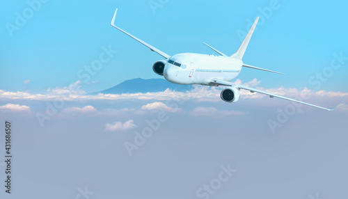 A passenger airplane flying over the clouds and a mountain peak in the background