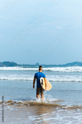 Surfer z deską surfingową na tle oceanu, mężczyzna uprawiający zdrowe sporty wodne.