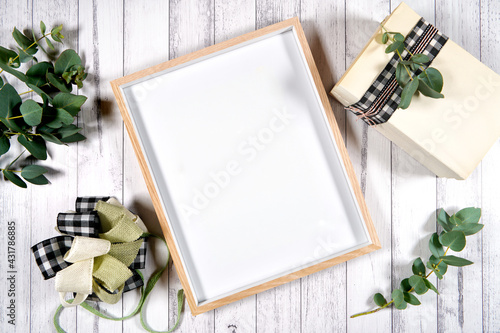 Artwork poster print wood frame. On-trend farmhouse theme flatlay craft product mockup with farmhouse style decor, stack of books, and bow on a white wood background. Negative copy space.