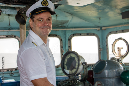 A captain standing in the wheelhouse of ship and looking to camera.