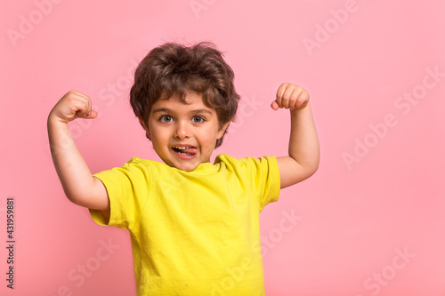 Funny little sportive kid boy in yellow shirt, showing his muscles. Happy strong nerd kindergarten child showing bicep. Dream, confidence, success, possible, innovation. Go back elementary school.