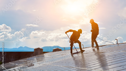 Solar roof technicians were washing and cleaning the surface of the solar panels with water, brush and mop on the roof of the building.