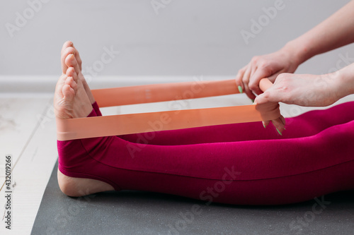 Resistance band exercise at home. Woman doing pilates workout using elastic strap pulling with arms for shoulder training on yoga mat indoors. Sport and healthy active lifestyle concept.