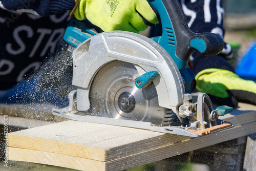 Carpenter working with a circular saw outside in sunny day. worker sawing wood board with electric circular saw. close-up