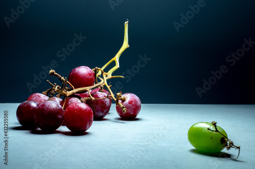 Racimo de uvas rojas y una uva verde asilada, idea de diferente, rechazo por ser diferente