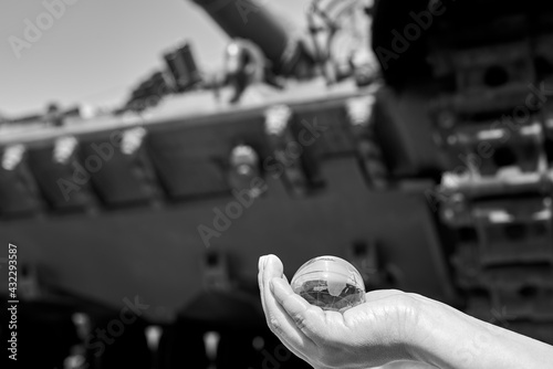 The glass globe of planet Earth in a woman's hand under the tracks of the tank.