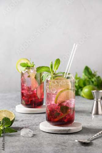 Two blueberries mojito with lime, mint and ice cube on gray background. Vertical format.