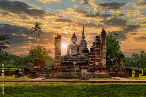 Buddha statue and pagoda Wat Mahathat temple with dramatic syk sunset, Sukhothai Historical Park, Thailand
