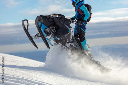 snowmobile. a guy rides a snow bike in the mountains against the backdrop of a ridge of rocks and a snow-covered valley. prof snowmobiler stands on a track with snow swirls.
