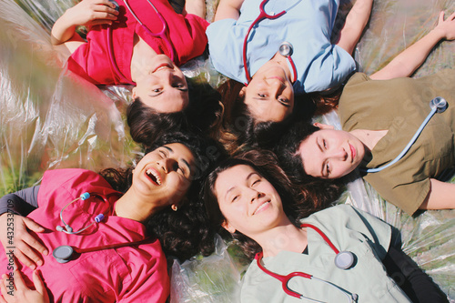 Group portrait of doctor / medical student / healthcare worker women smiling and happy outdoors in scrubs with stethoscopes 
