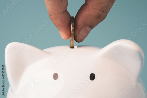 Hand putting coin to white piggy saving money, financial banking and bank deposit concept.