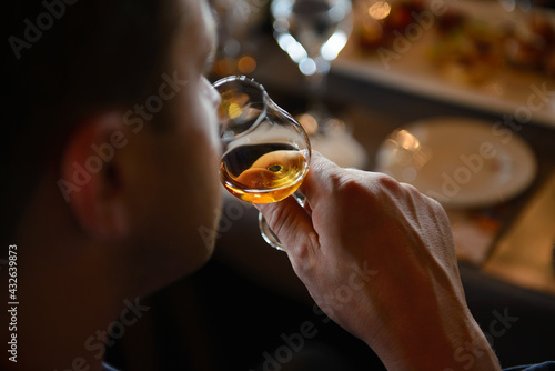 Man holding glass of cognac close to nose smelling the aroma