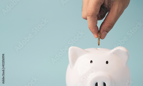 Hand putting coin to white piggy bank saving on blue background and copy space , Money saving for future investment and retirement concept.