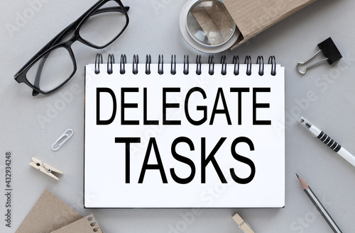 delegate tasks. Gray background. text on notepad near glasses with pen and pencil. business layout.