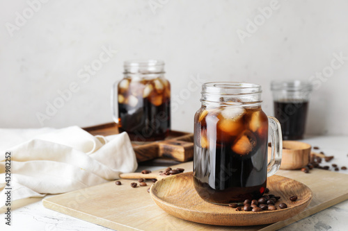 Mason jars of tasty cold brew and coffee beans on white background