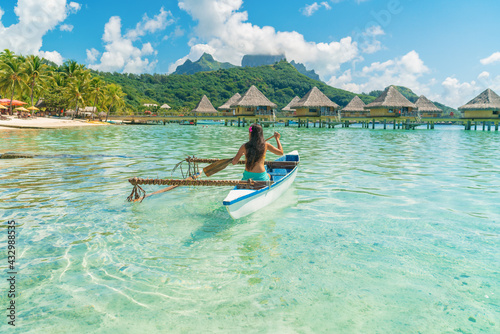 French Polynesia Tahiti travel vacation concept. Outrigger Canoe polynesian watersport sport woman paddling in traditional vaa boat. Water leisure activity, Bora Bora overwater bungalow resort hotel.