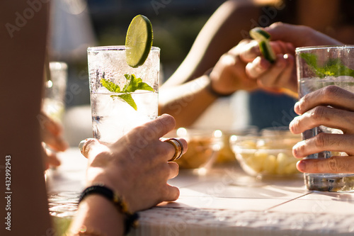 Hands holding a fresh alcoholic long drink cocktail on a table. Gathering of friends in an outdoor pub in the summer.