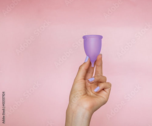 woman's hand holding a purple menstrual cup, on a plain pink background