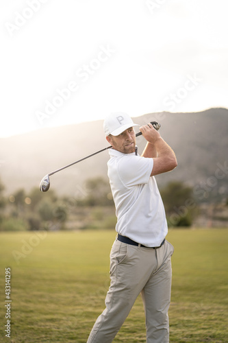 Golf player making a perfect swing on the golf course in the sunset.