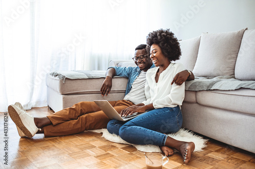 Young black couple sit on the floor using laptop, side view. People, leisure, mutliethnic relationship concept. Lovely mixed race couple spend free time at home, dressed casually, embrace