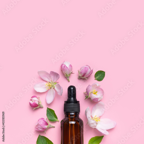 Clean brown glass cosmetic bottles with dropper, delicate spring flowers on pink background flat lay top view. Spring concept of natural organic cosmetics, beauty herbal product spa aroma oil. Mockup