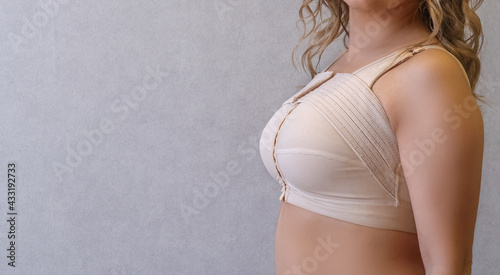 Young woman in beige compression bra bandage after breast augmentation surgery mammoplasty. banner. advertising. copy space