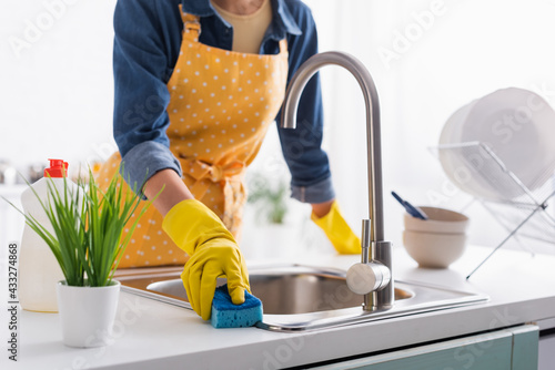 Cropped view of housewife with sponge cleaning sink in kitchen