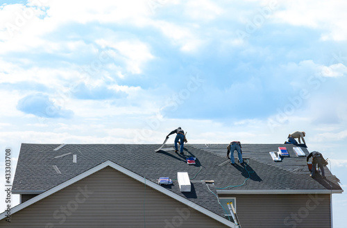 4 construction workers fixing roof against clouds blue sky, install shingles at the top of the house. Renovate, improvement, build home exterior by professional teamwork. Safety and protection concept