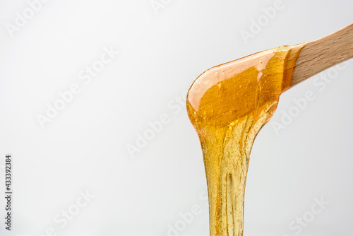 Liquid yellow sugar paste or wax for epilation on wooden stick or spatula closeup