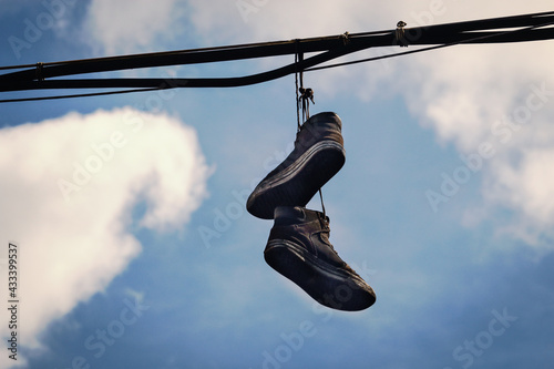 Two dirty old sneakers hanging on wires in blue sky with clouds