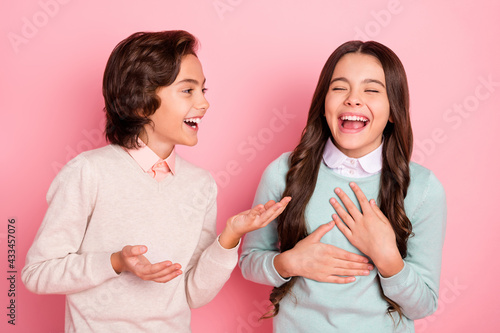 Portrait of attractive trendy cheerful kids boy sharing funny joke to girl laughing having fun isolated over pink pastel color background