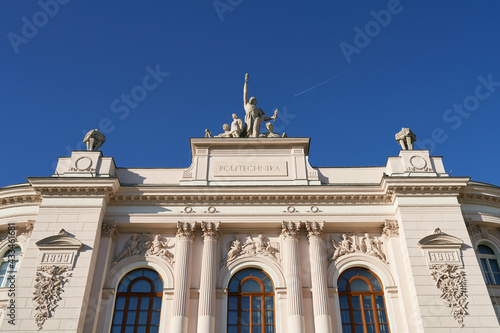 Facade top of the main building of Warsaw University of Technology on blue sky background with flying plane. Warsaw, Poland.