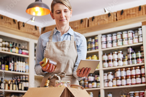 Female Owner Of Delicatessen Food Shop With Digital Tablet Preparing Online Grocery Order